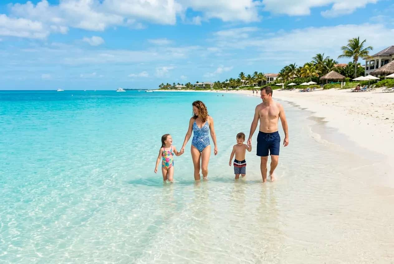 Shallow turquoise water at Grace Bay Beach in Turks and Caicos with young children wading in the calm surf